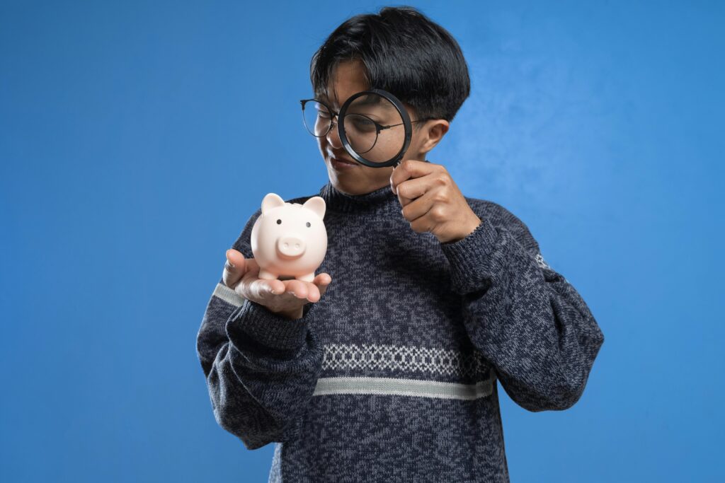 pexels-photo-12357424-12357424 A person closely examines a piggy bank with a magnifying glass, symbolizing financial scrutiny.